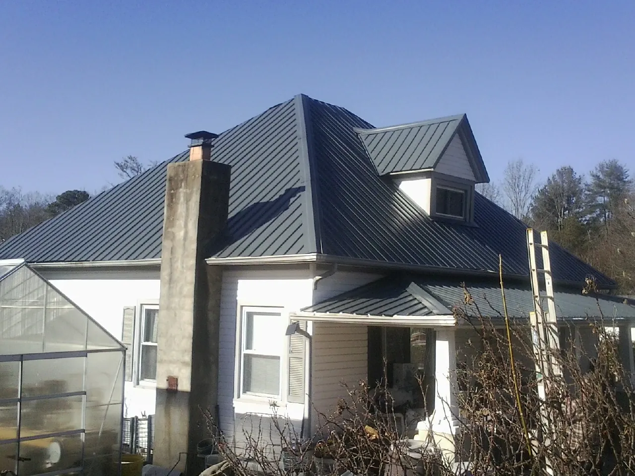 Dark blue standing seam metal roof on a white farmhouse with dormer — Slate & Tile Roof Repair by Roofing Brothers in Thurmond