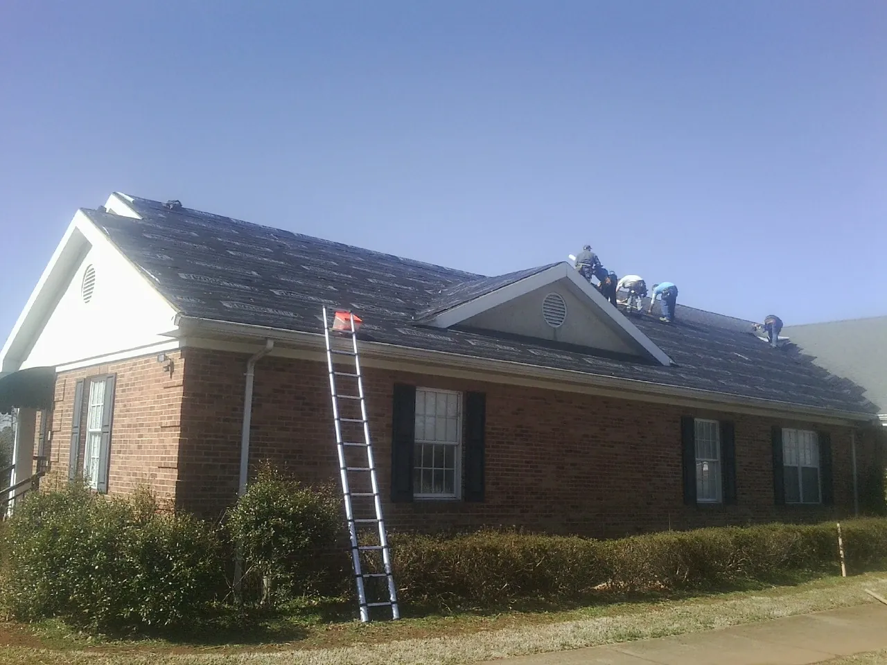 Crew tearing shingles off a brick ranch roof with a ladder set — Emergency Roof Repair work by our crew in Thurmond