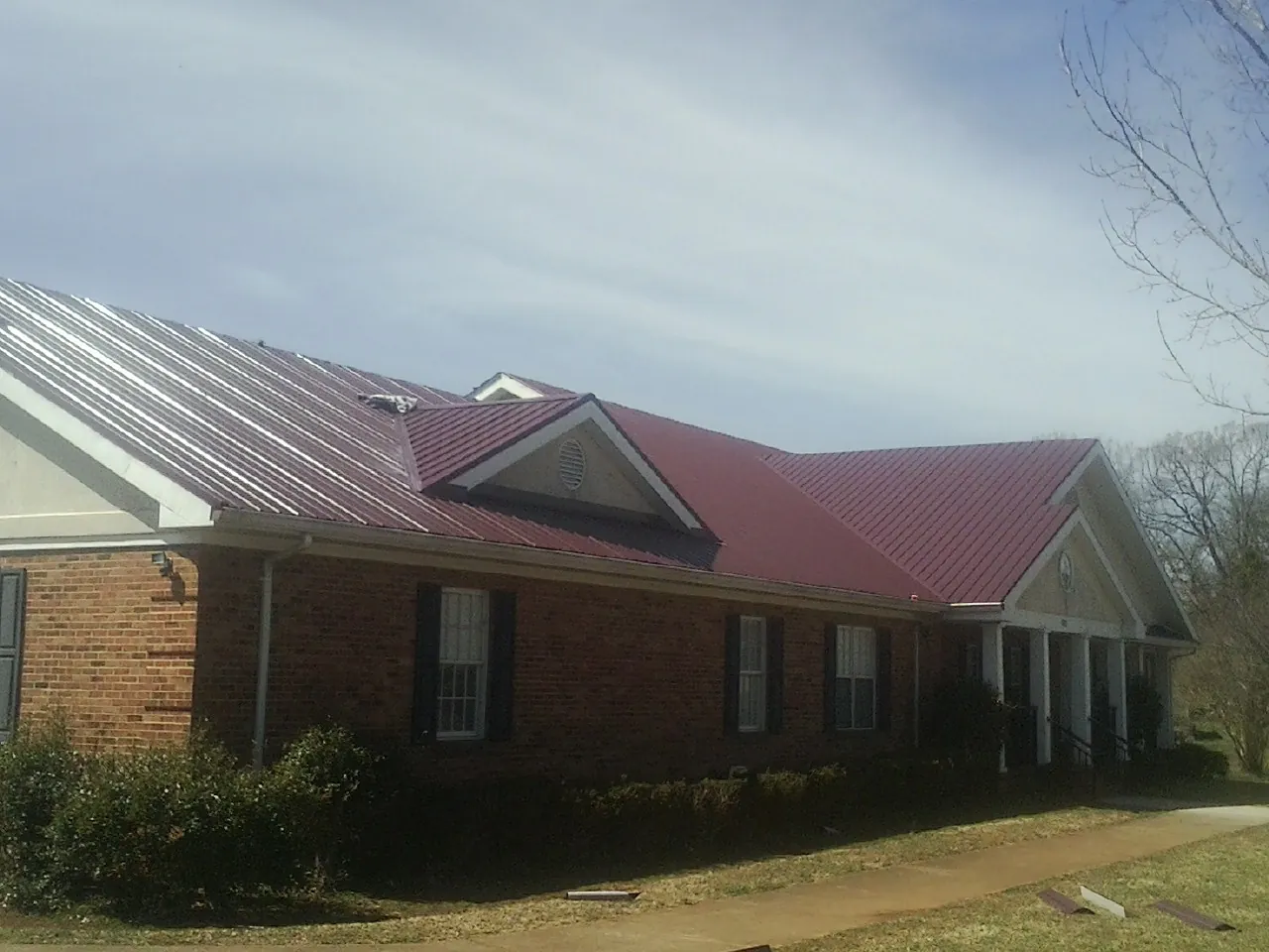 Red metal roof with gabled entries on a long brick building, from a Hail Damage Roof Repair job in Thurmond