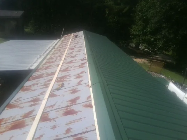 Old rusted panels beside newly installed green metal roofing — Wind Damage Roof Repair by Roofing Brothers in Thurmond
