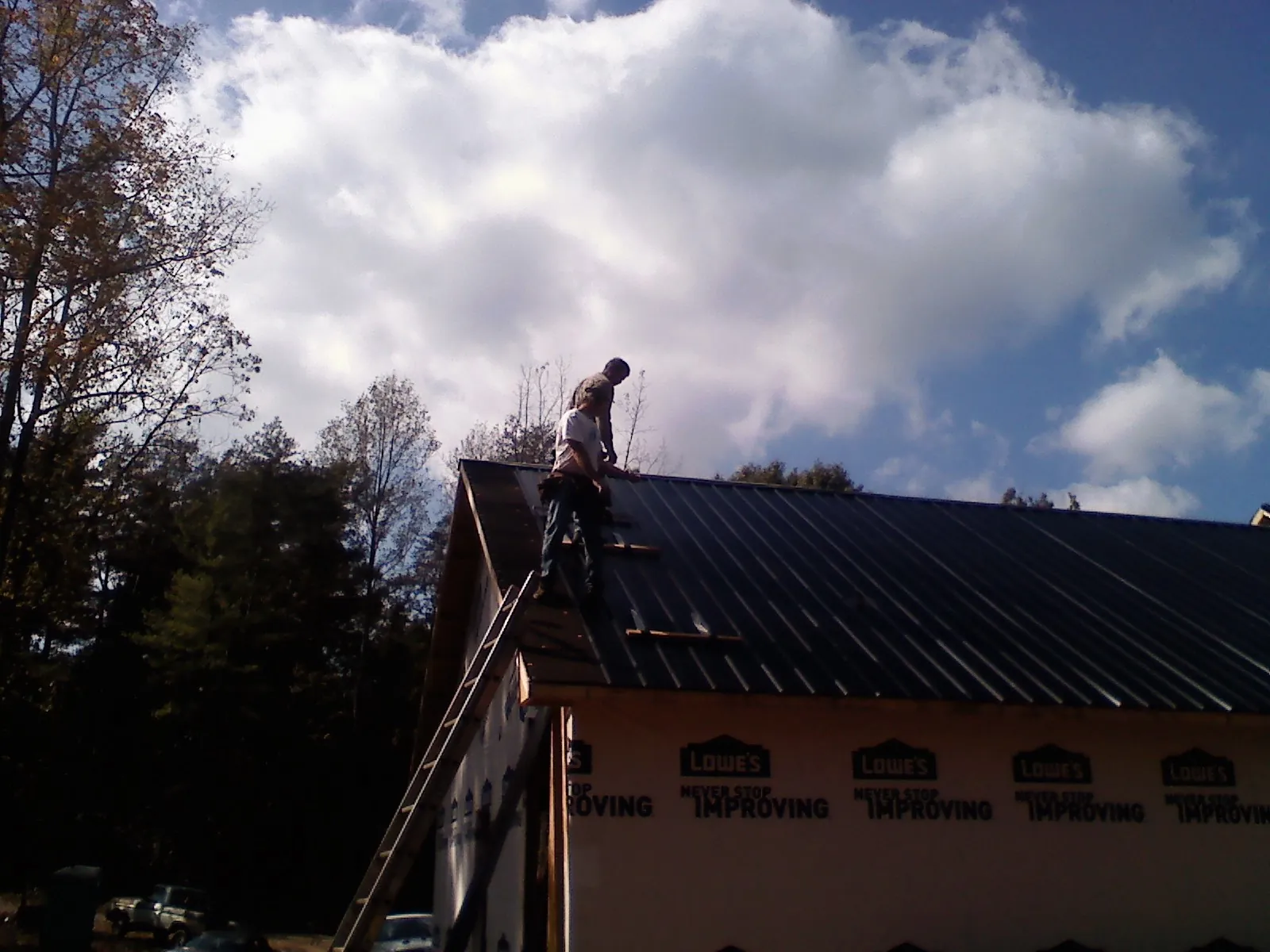 Roofer fastening dark metal panels high against a cloudy sky, from a Roof Inspection job in Thurmond